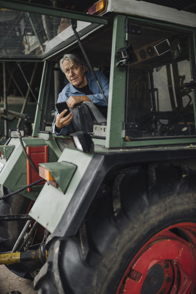 starszy mezczyzna trzymajacy smartfon na traktorze